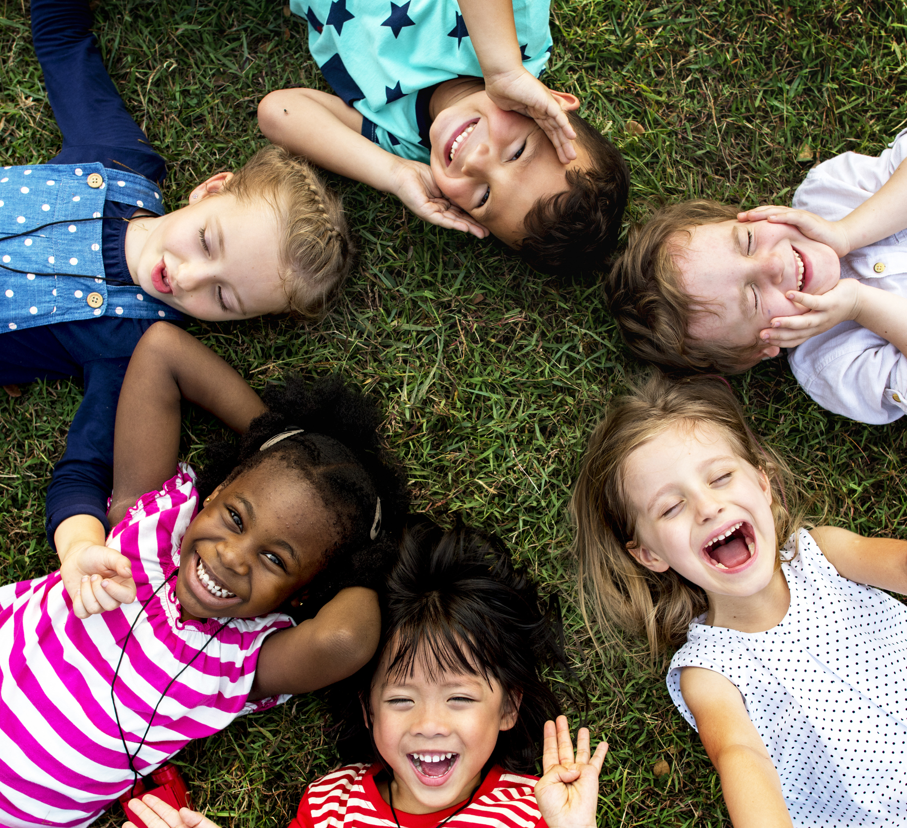A group of diverse children laying on the ground in a circle