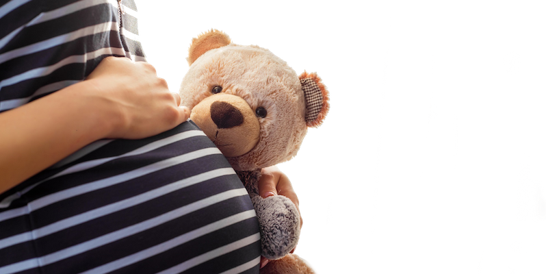 Pregnant woman holding a teddy bear close to her stomach