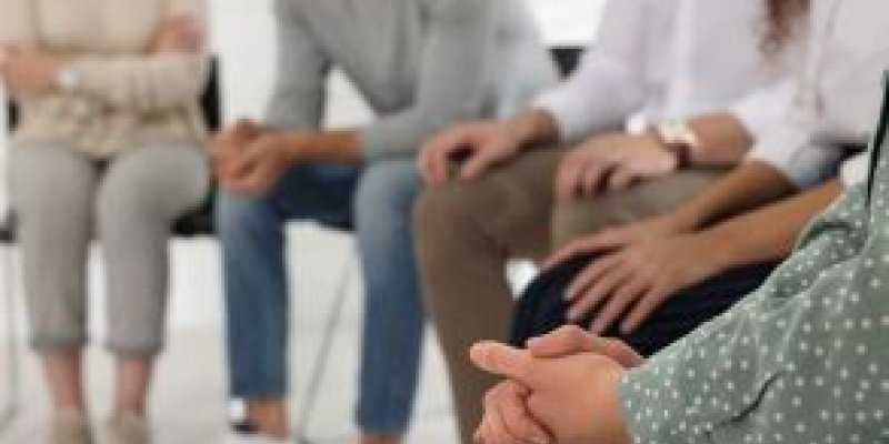 Shot of seated counselor and group of people from feet to neck