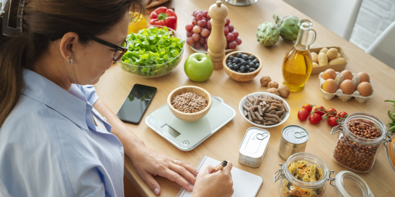 Woman writing at desk surrounded by fruits and vegetables